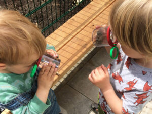 Zwei Kita Kinder schauen in ein Vergrößerungsglas