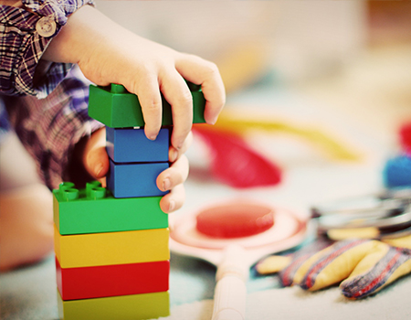 ein Junge , nur die Hände zu sehen spielt mit bunten Bauklötzern im Familienzentrum AlveBauklötzer