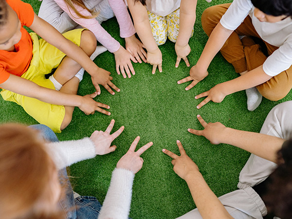 Kinder aus dem Ganztag inder Schule am Koppelweg sitzen im Kreis und zeigen mit ihren Fingern in die Mitte