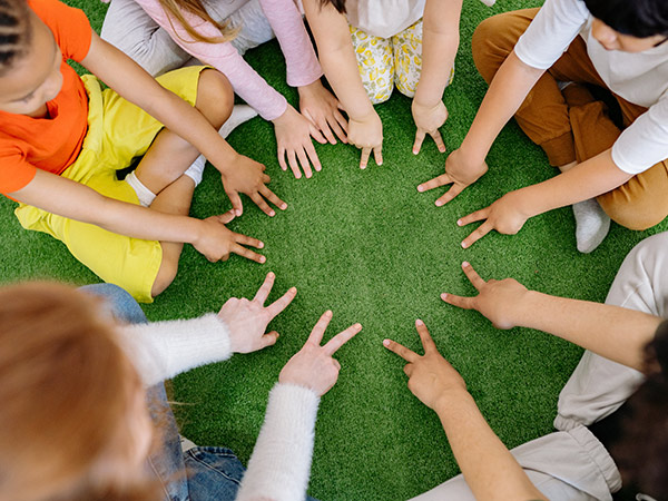 Grundschulkinder sitzen im Kreis auf einem grünen Boden