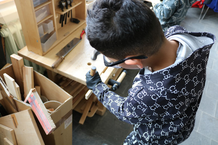 Ein Junge arbeitet mit Schraubenzieher und Hammer in der Lernwerkstatt