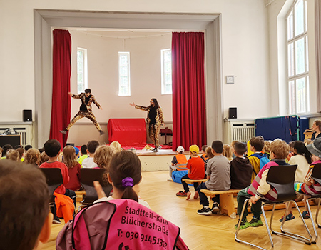 Siegrfied und Joy, die Zauberer im goldenen Palettenanzuf stehen auf einer Bühne, viele Kinder sitzen davor