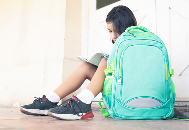 Mädchen sitzt mit grünem Schulranzen auf dem Boden