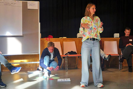 Drei Teilnehmende eines Workshops der TWG-Tagung in Berlin bei einem Workshop, ein Mann sortiert Karten auf dem Boden, eine Frau spricht